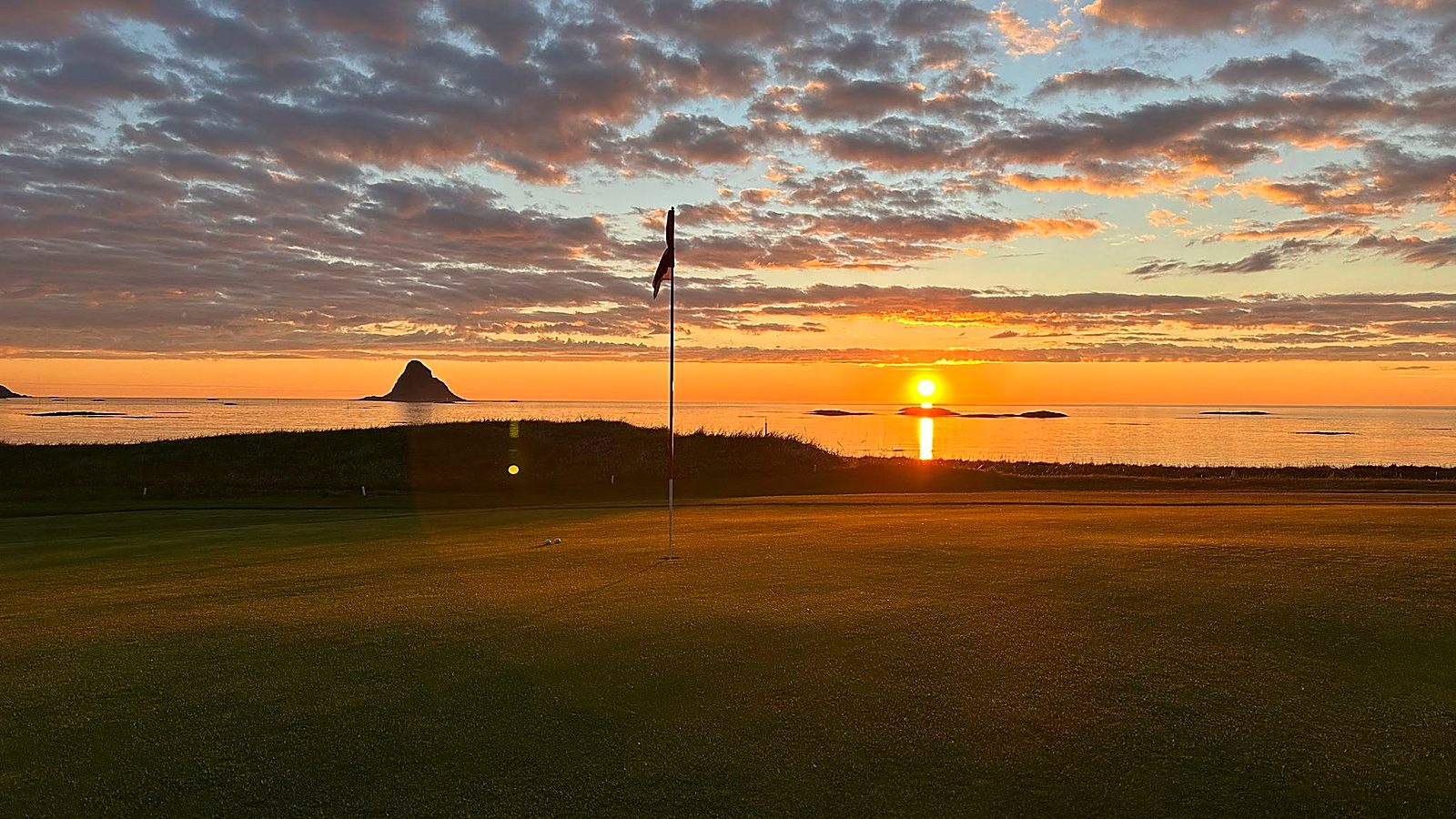 Solnedgang over havet med Bleiksøya og golfflagget i forgrunnen